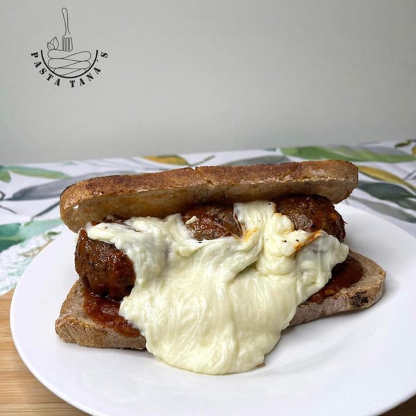 A meatball sub with melted mozzarella cheese and marinara sauce on a white plate.