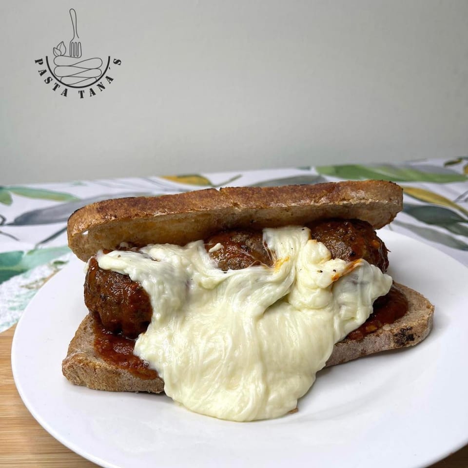 A meatball sub with melted mozzarella cheese and marinara sauce on a white plate.