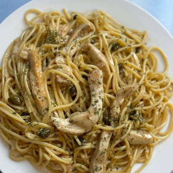 Pasta Tana's spaghetti with chicken, capers, and herbs in a creamy sauce on a white plate.