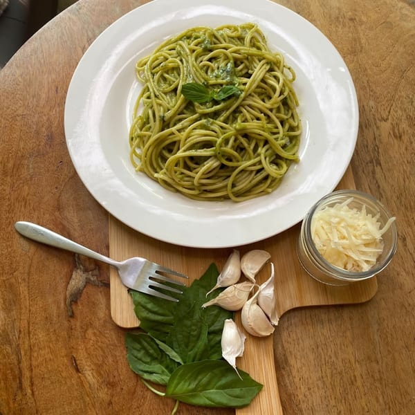 Pasta Tana's pesto spaghetti with basil, garlic, and grated cheese on a wooden table.