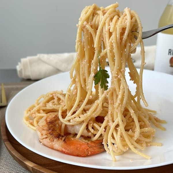 Fork lifting spaghetti with tiny orange roe and a large grilled shrimp on a white plate.