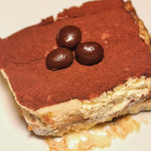 A close-up of a slice of tiramisu with cocoa powder and three chocolate-covered espresso beans.