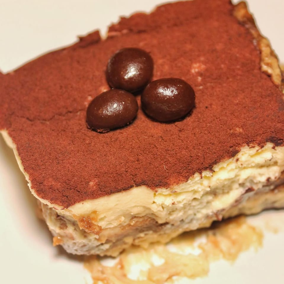 A close-up of a slice of tiramisu with cocoa powder and three chocolate-covered espresso beans.
