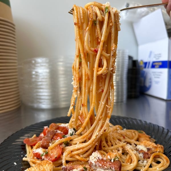 Fork lifting a large portion of spaghetti with red sauce, tomatoes, and cheese from a black plate.