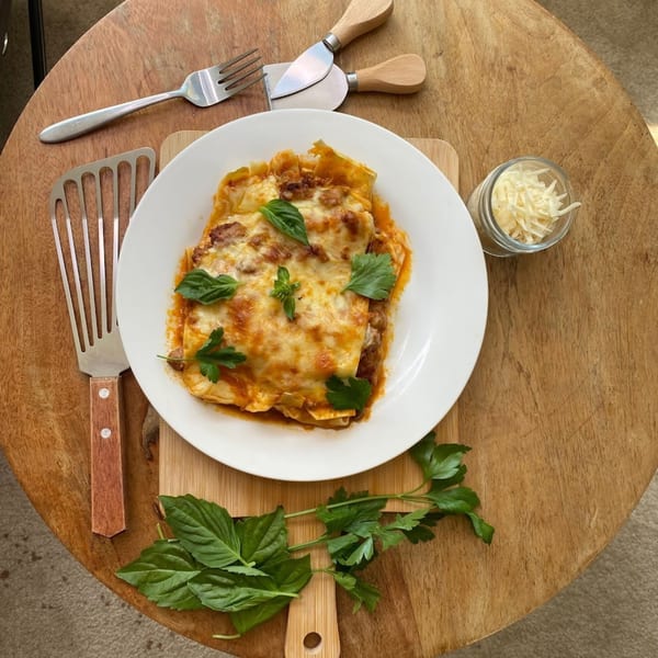 Pasta Tana's lasagna with melted cheese and fresh herbs on a wooden table with utensils.