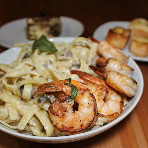Creamy fettuccine pasta with mushrooms and grilled shrimp, garnished with basil, at Pasta Tana's.