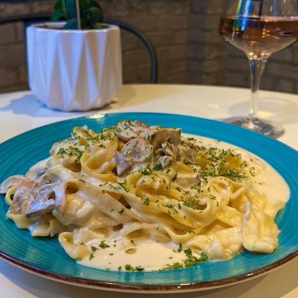 Creamy mushroom tagliatelle pasta with parsley on a blue plate, with a glass of white wine.