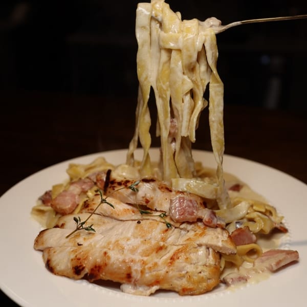 Creamy fettuccine pasta with grilled chicken, bacon, and thyme, twirled on a fork.