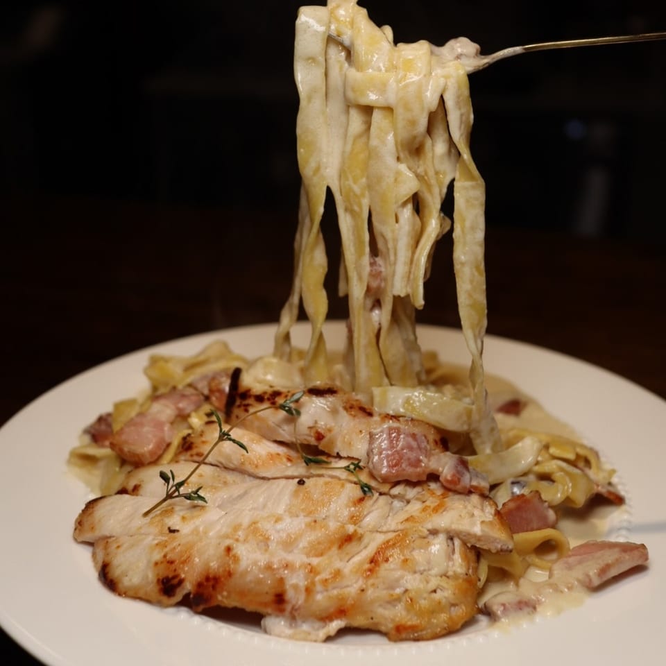 Creamy fettuccine pasta with grilled chicken, bacon, and thyme, twirled on a fork.