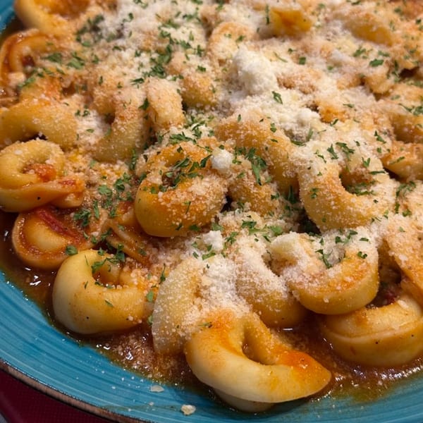Close-up of Pasta Tana's tortellini pasta with red sauce, parmesan cheese, and parsley on a blue plate.